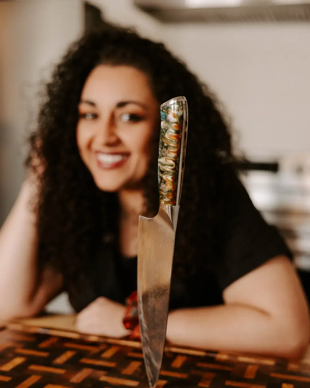 Nicolette Durham, owner of The Backyard Hostess, smiling behind a chef's knife on a wooden cutting board.